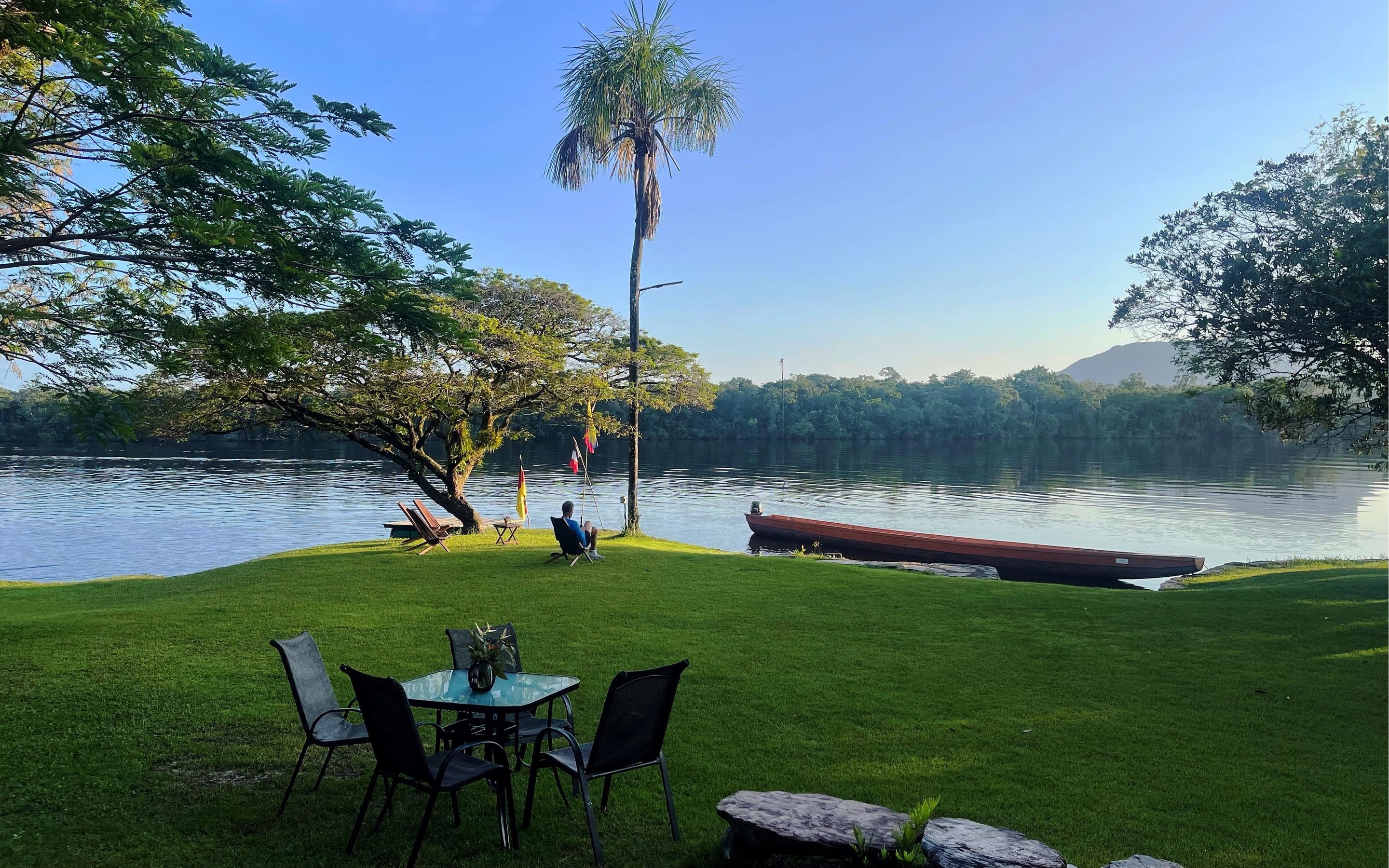 Jardín con mesa frente a la laguna, una palmera y una curiara
